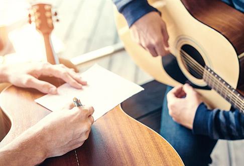 two people writing music and playing guitar